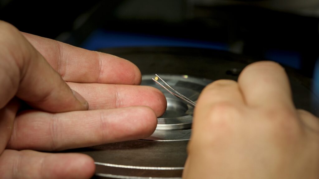 A person’s hand holding the world’s smallest coin between a pair of tweezers