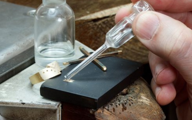 Image of the touchstone test — rubbing metal across a dark stone and comparing the streak color to known alloys
